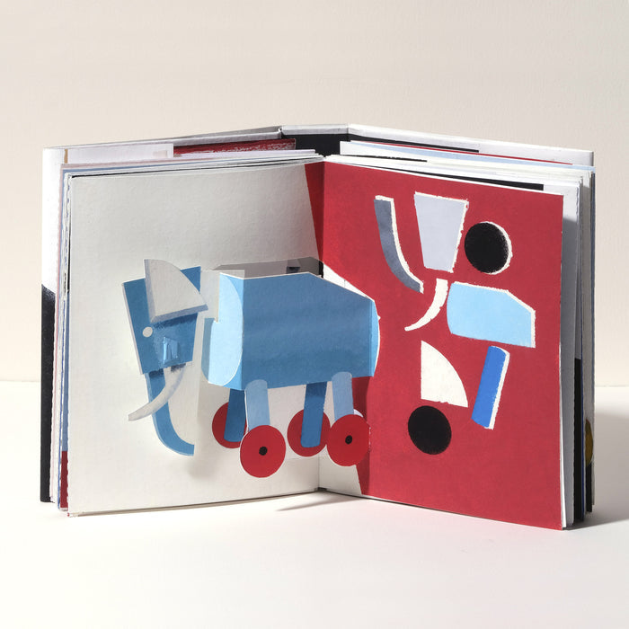 Open art book featuring a playful 3D pop-up blue elephant with wheels, paired with bold geometric abstract artwork in red, black, white, and blue on the opposite page.