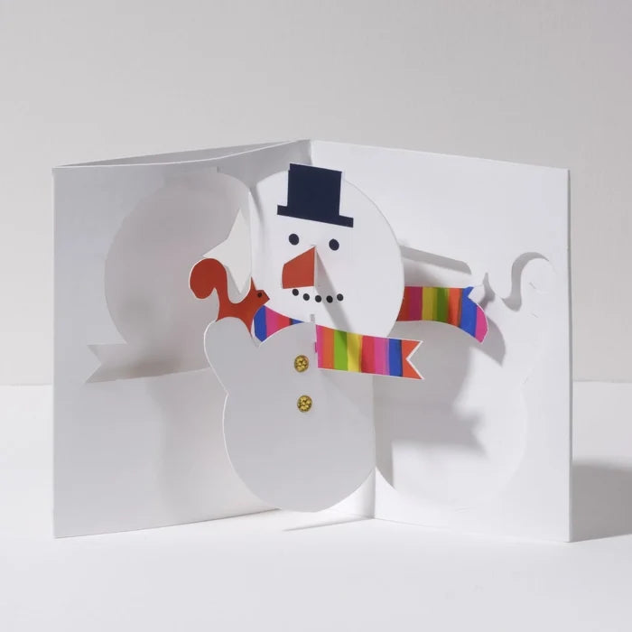 Open 3D pop-up Christmas card featuring a cheerful snowman with a black top hat, orange carrot nose, and rainbow striped scarf in a festive modern paper art design.