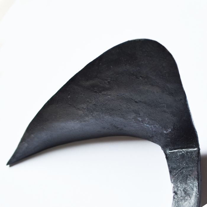 Close-up of a hand-forged large weeding hoe blade in dark steel, shown on a clean white background to highlight its curved shape, sharp edge, and artisan craftsmanship.