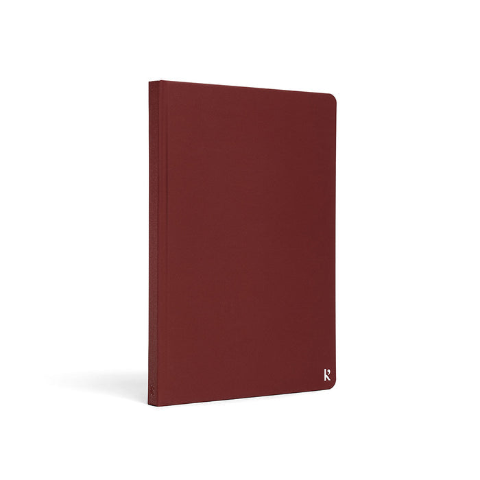Karst A5 hardcover stone paper notebook in deep red with rounded corners and subtle logo detail, standing upright on a light gray background.