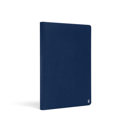 Karst A5 hardcover stone paper notebook in navy blue with rounded corners and subtle logo detail, standing upright on a light gray background.