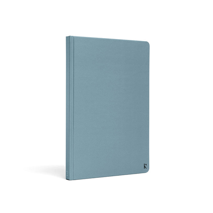 Karst A5 hardcover stone paper notebook in soft blue with rounded corners and minimalist logo detail, standing upright on a light gray background.