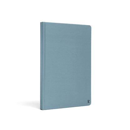 Karst A5 hardcover stone paper notebook in soft blue with rounded corners and minimalist logo detail, standing upright on a light gray background.