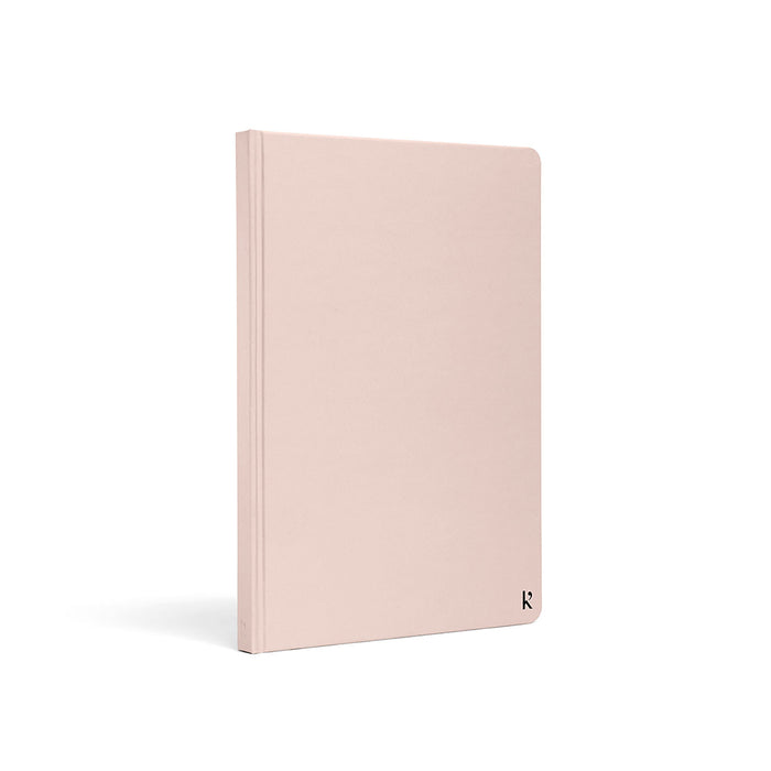 Karst A5 hardcover stone paper notebook in soft blush pink with rounded corners and minimalist logo detail, standing upright on a light gray background.