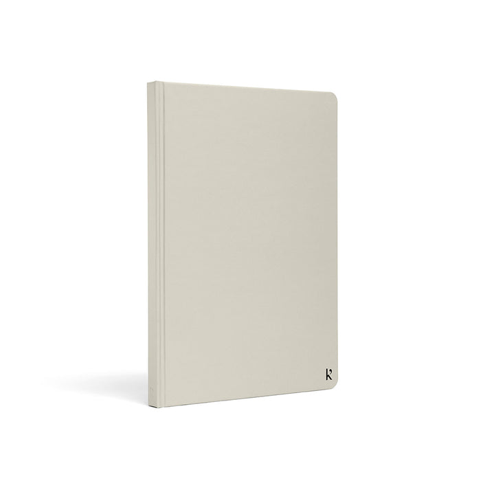 Karst A5 hardcover stone paper notebook in stone grey with rounded corners and minimalist logo detail, standing upright on a light gray background.