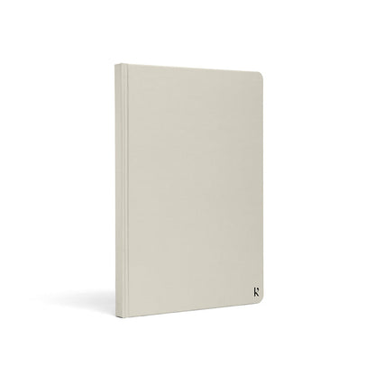 Karst A5 hardcover stone paper notebook in stone grey with rounded corners and minimalist logo detail, standing upright on a light gray background.