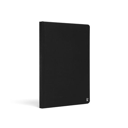 Karst A5 stone paper notebook with a black hard cover, shown at a three-quarter angle on a white background, featuring a minimalist design with a subtle embossed Karst logo in the lower corner.