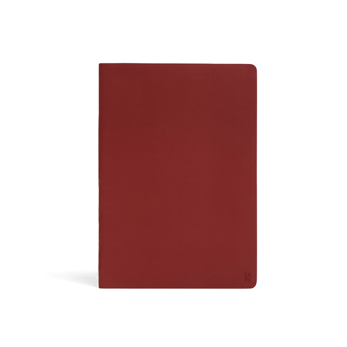 Karst A5 softcover stone paper notebook in deep red (Pinot) with rounded corners and subtle embossed logo, standing upright on a light gray background.