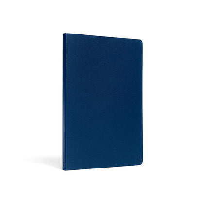 Karst A5 softcover stone paper notebook in navy blue with rounded corners and embossed logo, upright on a light gray background.