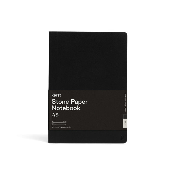 Karst A5 softcover stone paper notebook in black with branded wrap label, rounded corners, and minimalist design, standing upright on a light gray background.