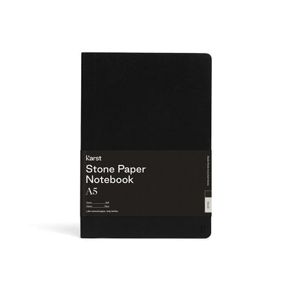 Karst A5 softcover stone paper notebook in black with branded wrap label, rounded corners, and minimalist design, standing upright on a light gray background.