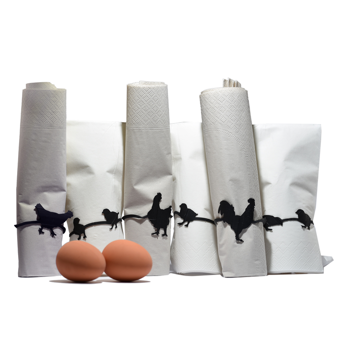 Black chicken-shaped rubber bands wrapped around paper towel and napkin rolls, playful farm animal office and kitchen organizers displayed with two brown eggs.