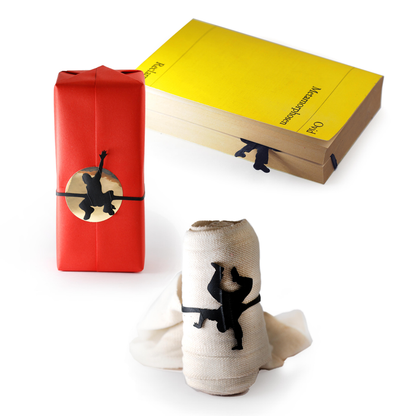 Black monkey-shaped rubber bands used to wrap a gift, hold a book page, and secure a rolled cloth, playful animal-shaped organizers for gift wrapping, bookmarks, and household use.