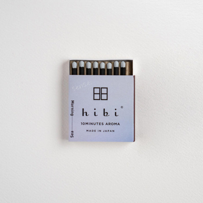 A small matchbox of Hibi 10minutes Aroma matches on a clean white textured background. The matchbox features a light lavender cover with black text and logo, and the matches inside have white tips and dark stems.