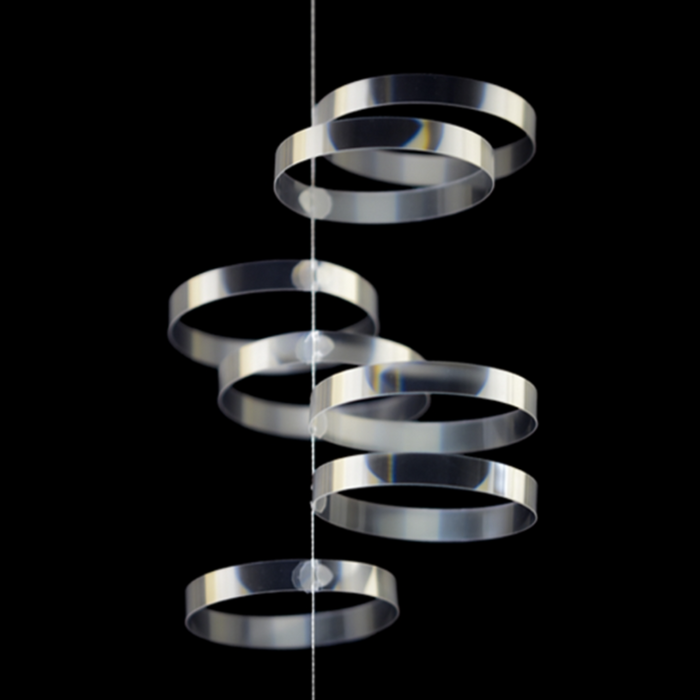 Minimalist hanging mobile made of transparent spiral rings suspended on a vertical string, modern kinetic decor with a sleek geometric design against a black background.
