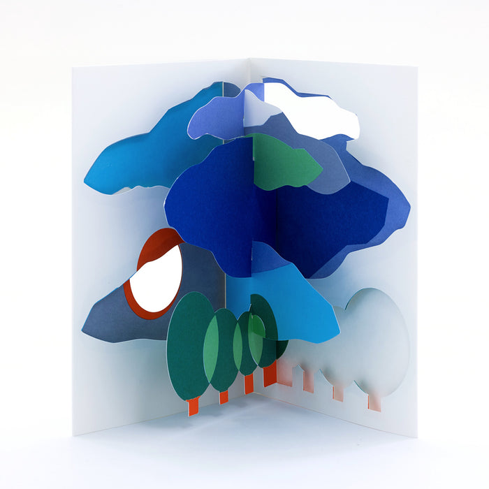 Open 3D pop-up greeting card featuring a stylized blue tree with layered foliage, green leaves, clouds, and a rising sun in a modern abstract paper art landscape design.