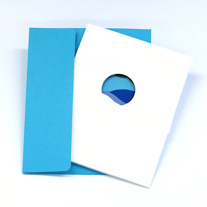 Minimalist greeting card with a circular landscape cutout on a white cover, paired with a light blue envelope in a clean modern stationery presentation.
