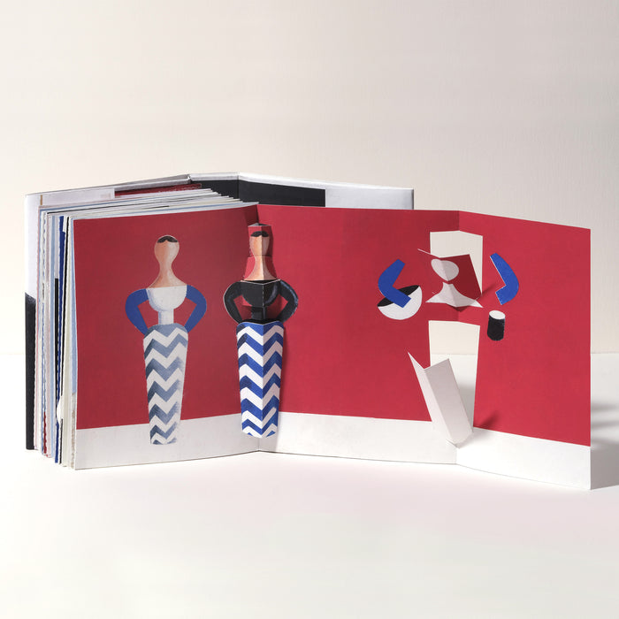 Open art book featuring a 3D pop-up fashion scene with stylized dolls in blue and white chevron dresses against a bold red background, showcasing playful geometric paper art and modern design.