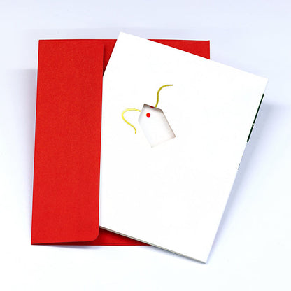 Minimalist Christmas greeting card with a small gift tag illustration on a white cover, paired with a bright red envelope in a clean festive stationery presentation.