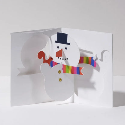 Open 3D pop-up Christmas card featuring a cheerful snowman with a black top hat, orange carrot nose, and rainbow striped scarf in a festive modern paper art design.