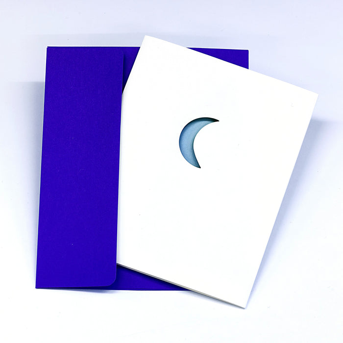 Minimalist Christmas greeting card with a crescent moon detail on a white cover, paired with a deep purple envelope in a clean winter holiday stationery presentation.