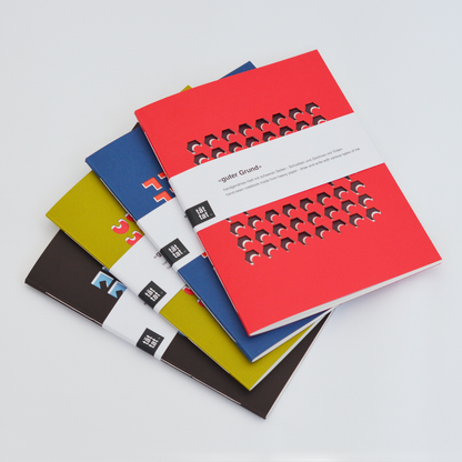 Colorful TÄT-TAT notebooks with geometric cutout covers stacked together, modern designer notebooks for writing, sketching, and creative journaling.