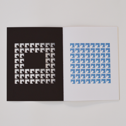 Open TÄT-TAT notebook showing geometric die-cut cover pattern with blue printed design on inner page, modern designer notebook for writing, sketching, and creative journaling.