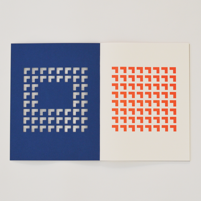 Open TÄT-TAT designer notebook with blue die-cut cover revealing orange geometric pattern on the inner page, modern creative notebook for writing, sketching, and journaling.