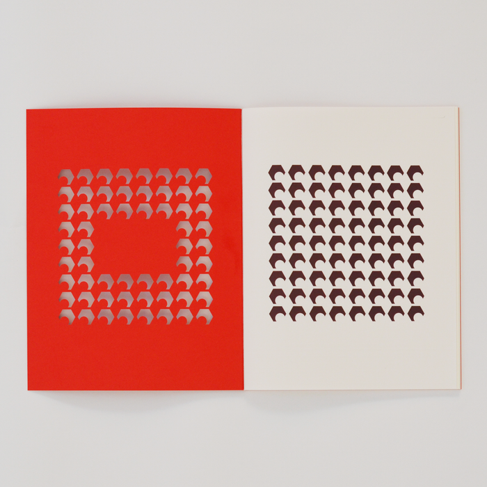 Open TÄT-TAT designer notebook with red die-cut cover revealing brown geometric pattern on the inner page, modern creative notebook for writing, sketching, and journaling.