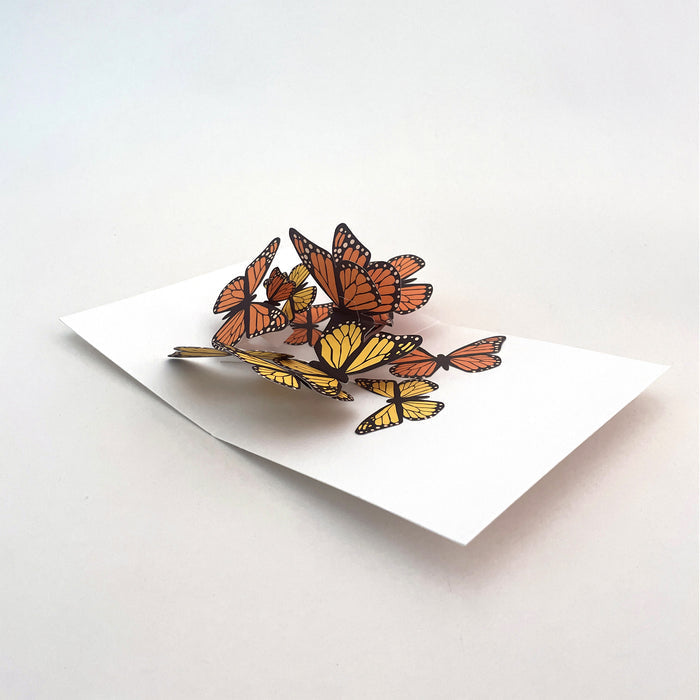 Open 3D pop-up greeting card featuring a group of orange and yellow monarch butterflies in motion on a white card base, elegant paper art card for birthdays, celebrations, and nature lovers.