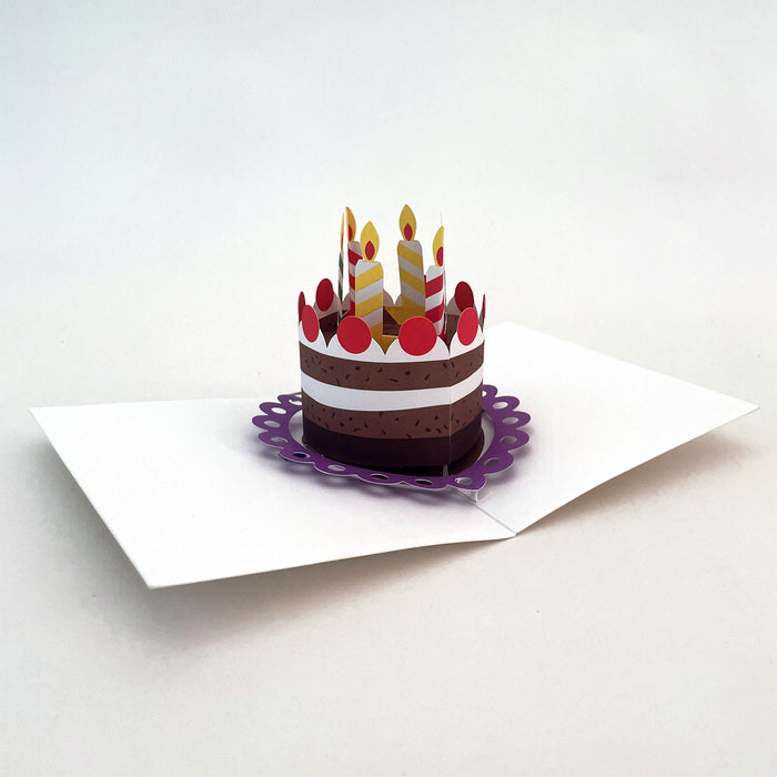 Open 3D pop-up birthday card featuring a layered cake with striped candles and red decorations on a white card base, festive paper art greeting card for birthdays and celebrations.