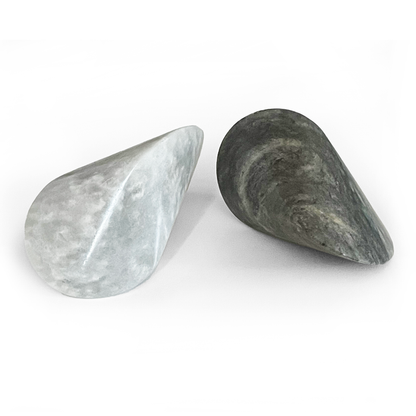 Set of two sculptural oloid objects in light gray and dark stone finishes, displayed on a clean white background in a minimalist modern decor product presentation.
