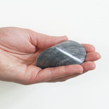Hand holding a smooth light gray marble oloid sculpture, shown against a clean white background to highlight its size, shape, and natural stone texture.