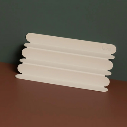 Stone colored, ridged Karst pen tray displayed on a warm brown surface against a muted green background, showcasing its minimalist, sculptural design.