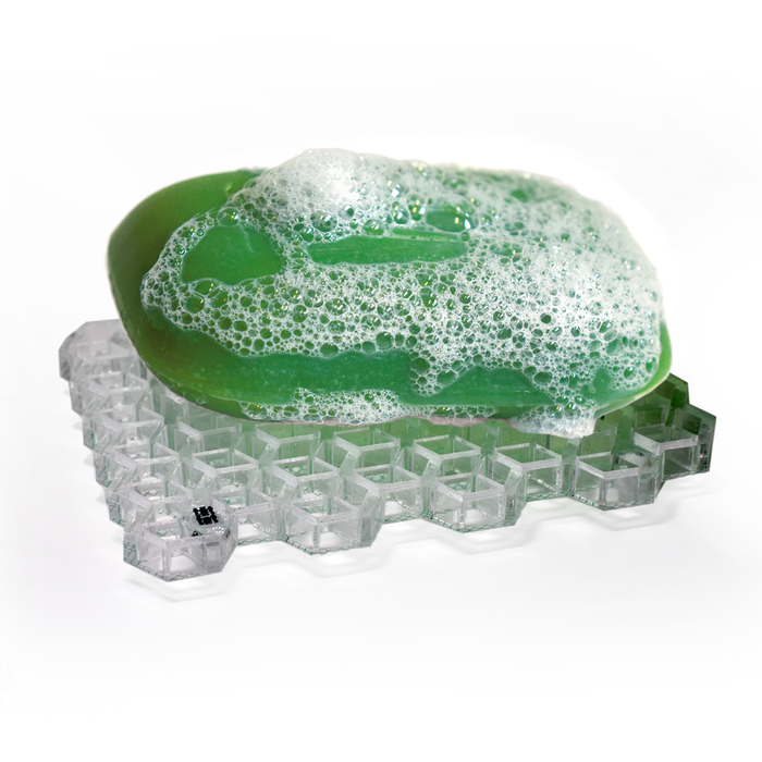 Green bar soap with foamy lather resting on a clear geometric soap dish, modern minimalist bathroom accessory for keeping soap dry and clean.