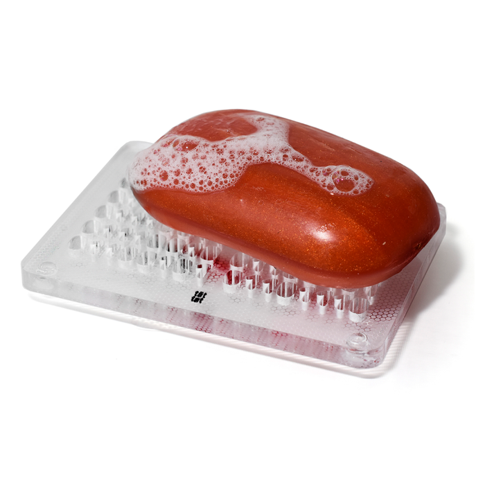 Orange bar soap with light lather resting on a clear minimalist soap dish, modern bathroom accessory designed to keep soap dry and extend soap life.