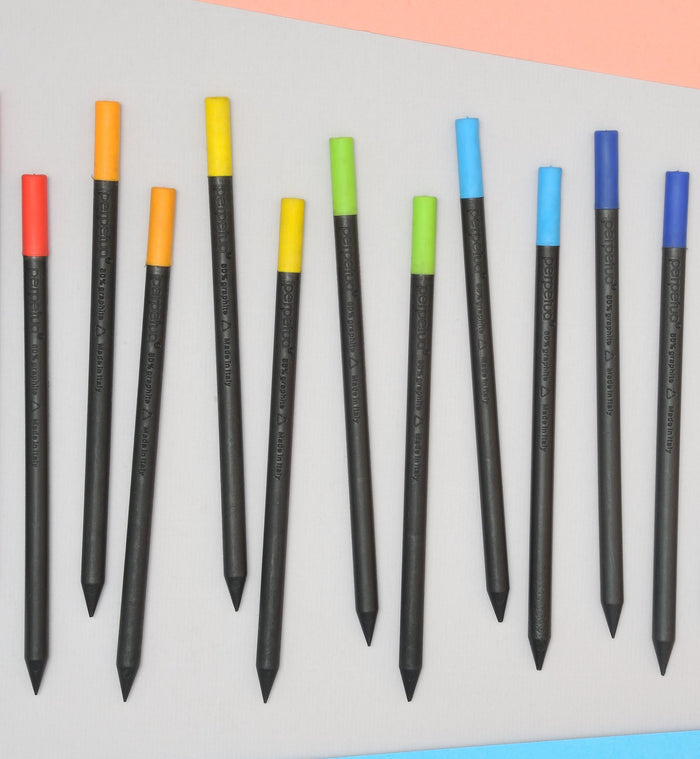 Set of Perpetua recycled graphite pencils with colorful eraser caps in red, orange, yellow, green, and blue, modern eco-friendly Italian stationery arranged on a minimalist background.