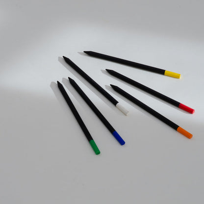 Set of black Perpetua recycled graphite pencils with colorful eraser caps in yellow, red, orange, green, blue, and white, arranged on a minimalist white background.