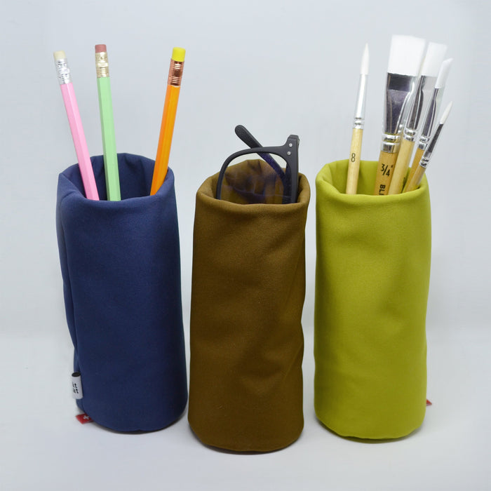 Three colorful soft desk organizers used as pencil holders, holding pencils, paintbrushes, and glasses—modern multifunctional stationery containers for office and creative workspace.