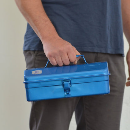 Person holding a blue Toyo steel toolbox by the top handle, shown closed with front latch.