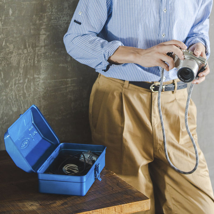 Open blue Toyo steel toolbox on a wooden table holding camera accessories, with a person standing nearby holding a camera.