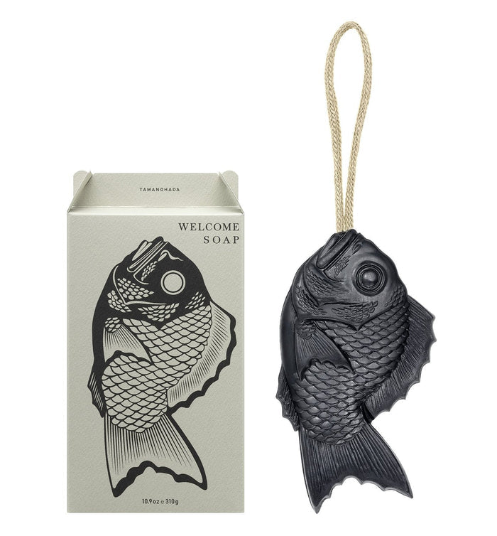 Black fish-shaped Tamanohada Welcome Soap with hanging rope and illustrated gift box packaging, decorative Japanese bath soap inspired by traditional tai fish.